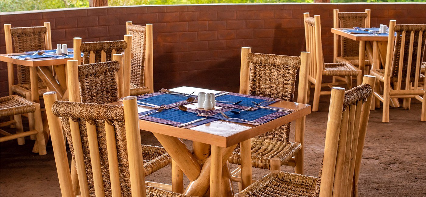 Des chaises tissées autour de tables dressées pour le petit déjeuner à Mara Safari Lodge Kidepo