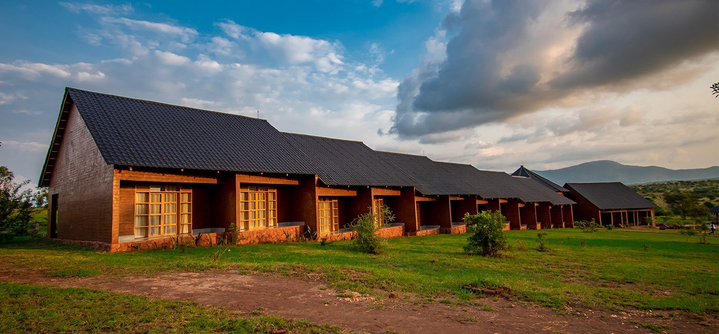 Une rangée de chambres chaumées avec les collines en arrière-plan à Mara Safari Lodge Kidepo